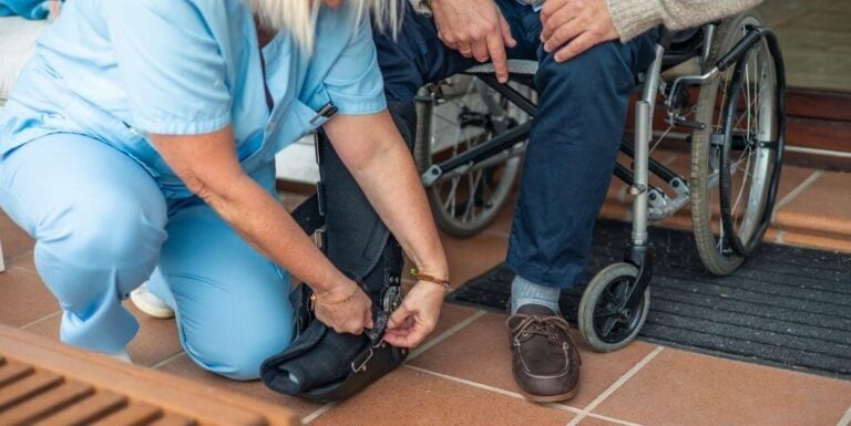 Female Nurse Helping Elderly Man Adjust Footwear at Assisted Living Facility