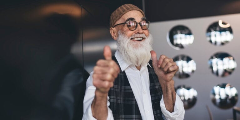 Elderly Man in Stylish Outfit Giving Two Thumbs Up Indoors at an Independent Living Facility