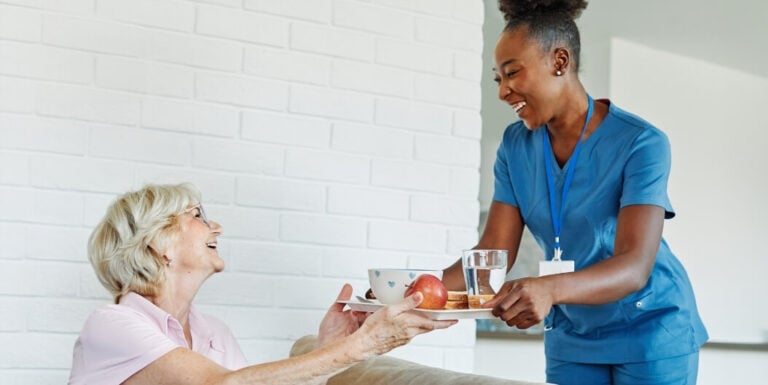Female Nurse Serving a Meal Tray to an Elderly Woman at an Assisted Living Facility